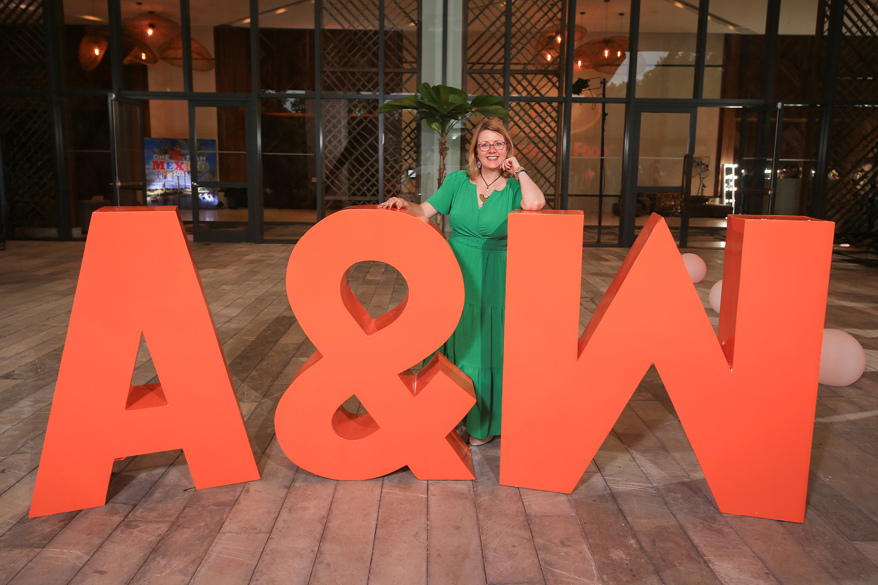 Betsy Schmandt wearing a green dress standing between large orange letters that spell &quot;A&amp;W&quot;