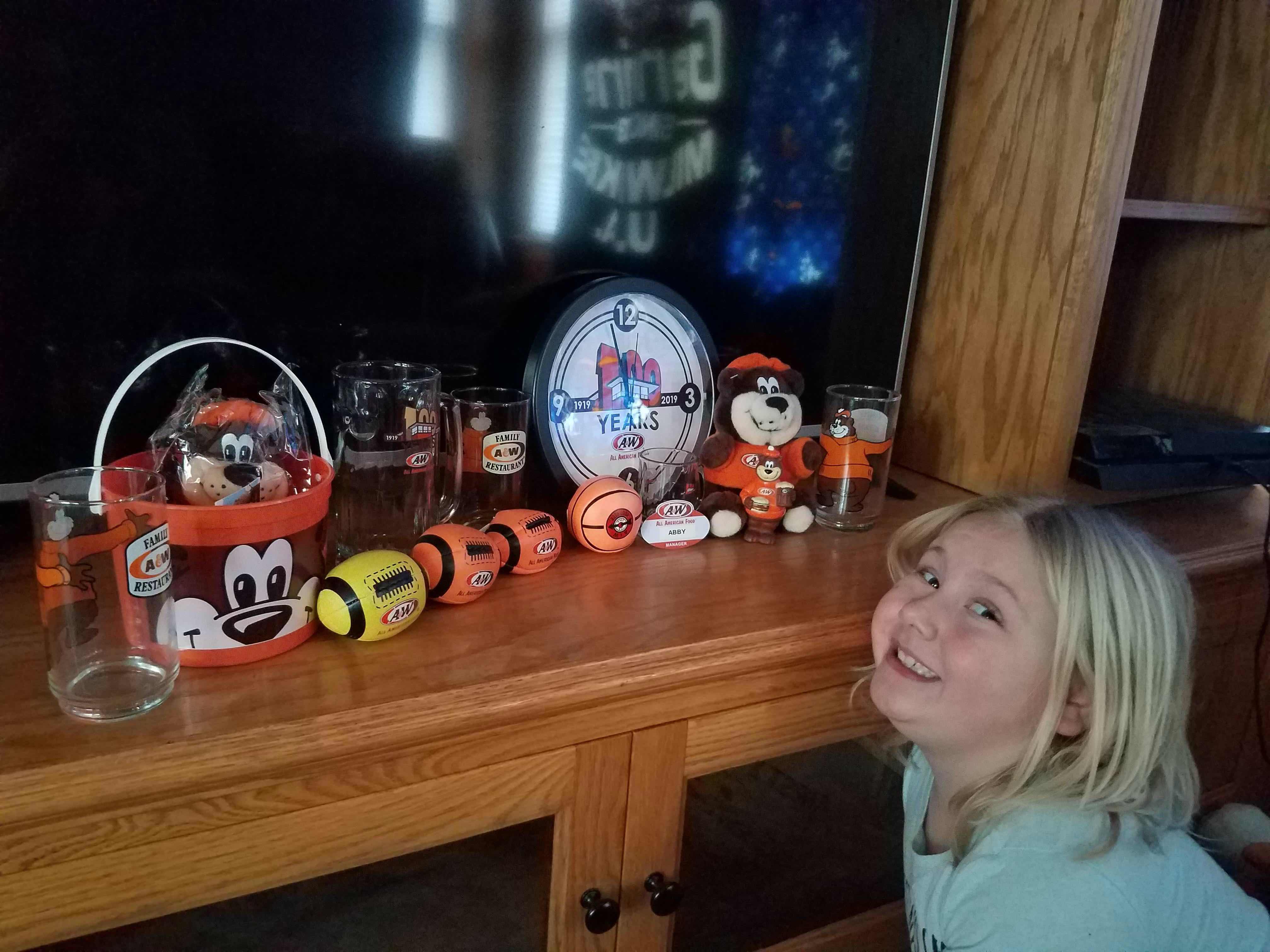 Photo of Abby sitting next to a shelf displaying various A&W Restaurants memorabilia